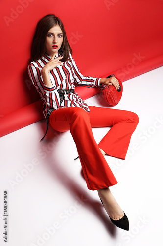 Zdjęcie XXL Moda piękny portret pięknej młodej kobiety. Czerwone spodnie, czerwona torebka, bluzka, czerwone tło