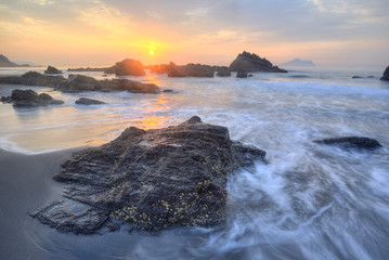 Wall Mural - Golden rays of rising sun light up the waves at a rocky beach in Yilan, Taiwan ~ A beautiful beach illuminated by the first ray of morning sunshine at Wai'ao, Ilan, Taiwan (Long Exposure Effect) 