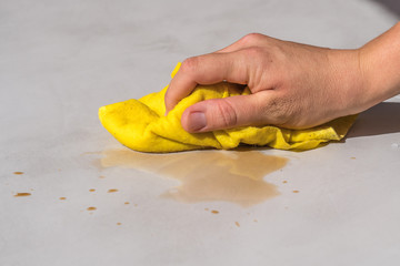 Wall Mural - woman's hand cleaning tea stain or spilled coffee on a cement floor with a yellow floor cloth dishcloth closeup