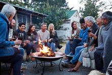 Group Of Friends And Family Relaxing Around Fire Pit At Farm