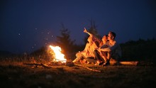 Young people sitting fire camp looking sky night outside nature pointing finger stars romantic having rest friends girls boy woman man three persons bonfire camping silence calm summer holidays warm