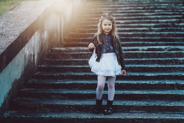 Stylish little girl in black leather jacket and white skirt posing outdoor