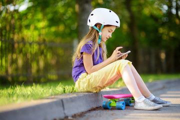 Wall Mural - Pretty little girl learning to skateboard on beautiful summer day in a park. Child enjoying skateboarding ride outdoors.