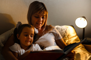 Wall Mural - mother and child girl reading a book in bed before going to sleep