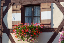 Half-timbered House With Window Shutters And Flowers