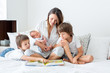 Young mother, read a book to her three children, boys, in the bedroom