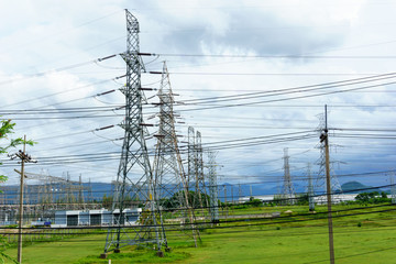 high voltage electricity pylon with transmission line near electricity station in the filed with cloudy sky.