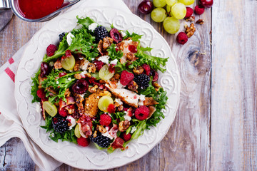 Delicious summer salad with mix of berries, nuts, feta chees, bacon and raspberry sauce on vintage background. Space for text