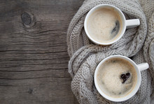 A Two Cup Of Hot Coffee With Foam Standing  On A Wooden Christmas Holiday Rustic Table  Background Wrapped In Warm Knit Wool Scarf. View From The Top. Space For Text.