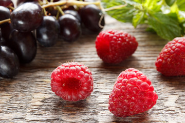 Berries of ripe raspberry and black grapes on a wooden background. Selective focus.