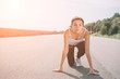 © estradaanton - Young woman athlete at starting position ready to start a race. Female sprinter ready for sports exercise on racetrack with sun flare.