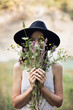 Giovane donna che sorriede nascosta da un mazzo di fiori di campo