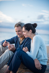 Poster - A couple sitting at the beach, looking at photos on a phone