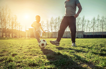 Father and son playing together with ball in football under sun