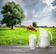 Glass and jug of milk against background of cow and pasture