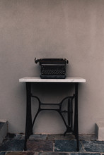 Old Vintage Typewriter Outdoors Against A Grey Wall On A Repurposed Sewing Machine Table