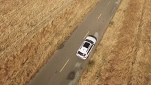 Aerial Footage Of White 4x4 SUV Car Driving On The Deserted Highway Between Dry Grass
