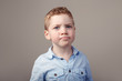 © anoushkatoronto - Closeup portrait of cute adorable blond redhead Caucasian little boy in blue shirt standing in studio on light white background. Child kid looking in camera with funny sceptical face expression