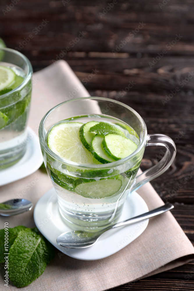 Delicious refreshing water with mint and cucumber in cup on wooden table