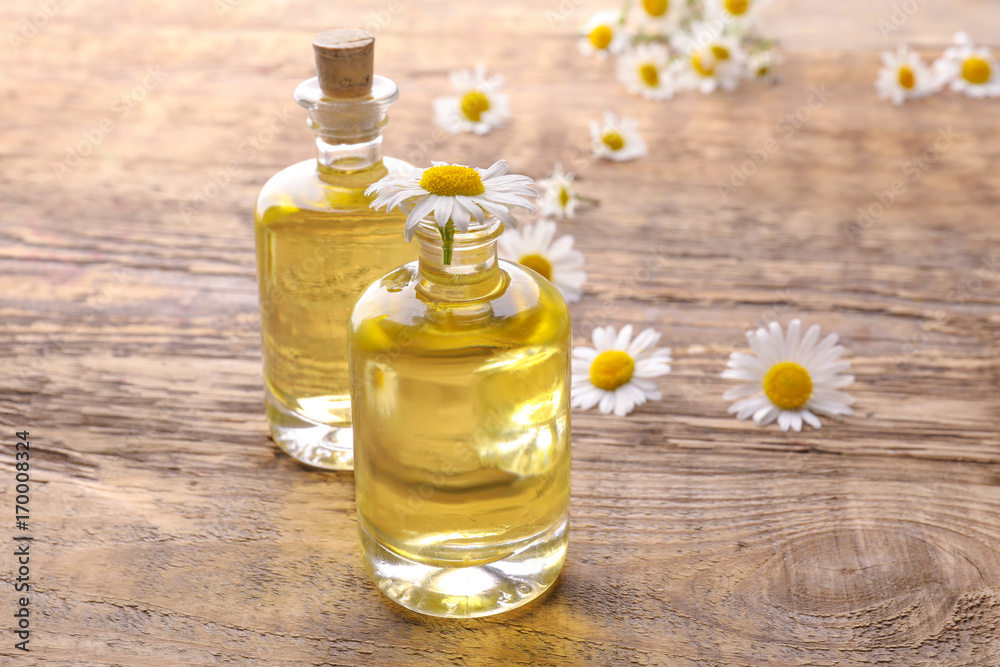 Bottles of essential oil and chamomile flowers on table