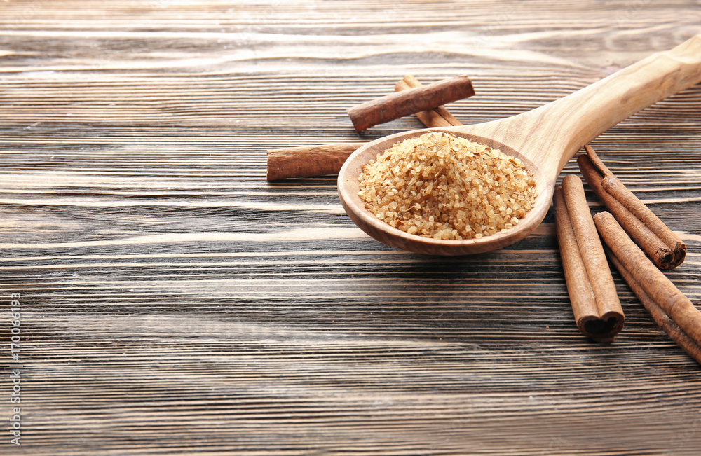 Composition with cinnamon sugar in spoon on wooden background