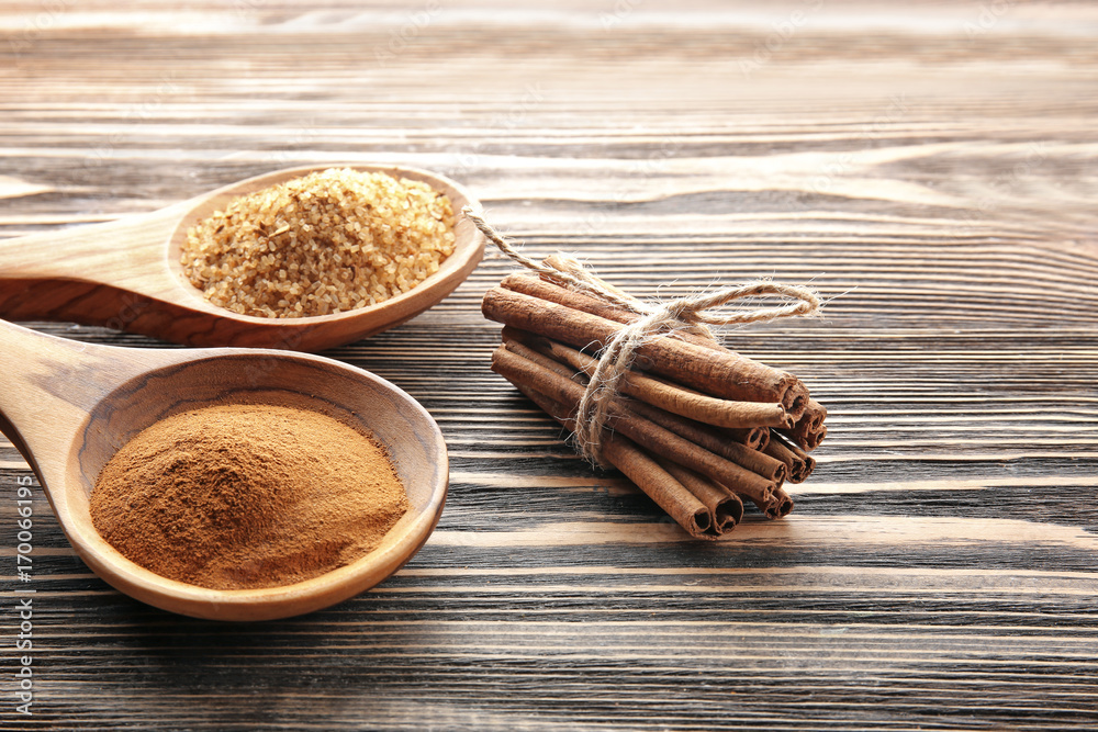 Composition with cinnamon sugar and powder in spoons on wooden background