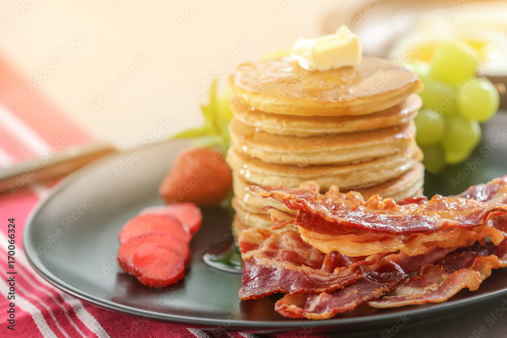 Tasty breakfast with pancakes, bacon and fruits on table