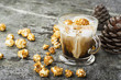 A glass of mouth-watering sweet milk coffee with a creamy foam topped with caramel crispy popcorn on a gray stone background. Selective focus.