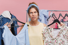 Clothing, Fashion, Style And People Concept. Stressed Young European Woman Having Indecisive And Frustrated Look While Choosing Dress To Wear On Party But Can't Find Anything Suitbale For Her