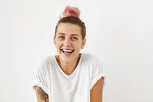 Positive Human Facial Expressions And Emotions. Headshot Of Beautiful Young Woman Of European Appearance With Pink Hair Knot And Tattooed Arm Resting Indoors, Having Carefree And Relaxed Look