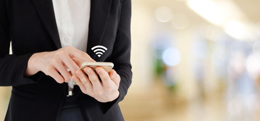 Wall Mural - Business woman hands using smart phone with wifi icon over blur office with bokeh light background, banner, business on phone