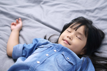 Wall Mural - closeup Asian children cute or kid girl wearing jeans sleeping and sweet dream with the smile on gray bed and bedtime in the bedroom at the home on warm white with space