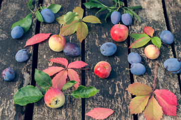 Wall Mural - Autumn fruits on an old wooden background. Plum, apples and red leaves of grapes