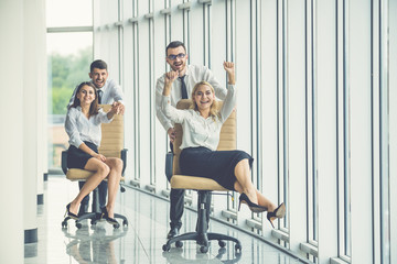 Wall Mural - The happy business people ride on chairs in the office hall