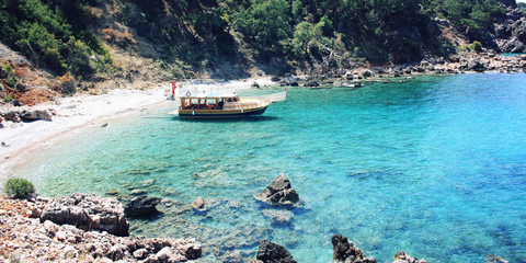 Passenger vessel waiting for tourists. Aged photo. Tourist boat in the small bay. Calm blue sea and green hills in Turkey. Walking the Turkey's Lycian Way. Wide photo for web site slider.