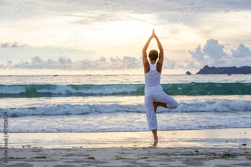 Fotografia Caucasian woman practicing yoga at seashore of tropic ocean