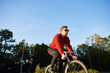 © Anatoliy Karlyuk - People, style, leisure, transportation and active lifestyle. Red-haired unshaven young European man in stylish clothes and shades riding his fixie on sunny summer day, trees and blue sky in background