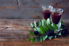 Blackberry Fruit Liqueur In Two Shot Glasses With Berries And Green Leaves
