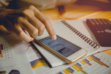 Hand of business woman touching screen of smart phone for searching business data. There is calculator beside her. Shallow depth of field. Focus at finger tip.