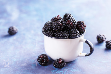 Wall Mural - Juicy fresh blackberries in a mug on blue background. Organic healthy berries. Selective focus