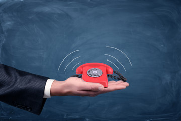Wall Mural - a businessman's palm hold a small red retro dial phone with lines showing soundwave emissions.