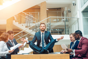 Wall Mural - Businessman wearing a suit doing Yoga on the table and other businessmans angry