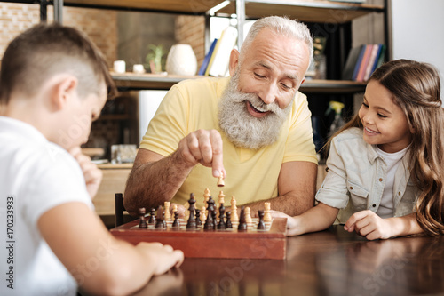 Cuadros en Lienzo Little girl watching her brother and grandfather play chess