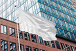 White blank flag waving in the wind in the urban background of modern buildings and skyscrapers. Perfect mockup to add any logo, symbol or sign