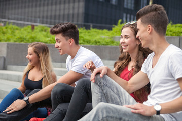 Wall Mural - Group of friends sitting together on stairs and laughing, city background