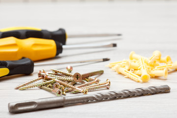 Screwdrivers, drill and screws on white wooden background