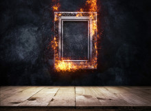 Fire Burning Silver Antique Picture Frame On Dark Grunge Wall With Wooden Table Top, Empty Ready For Product Display Or Montage.
