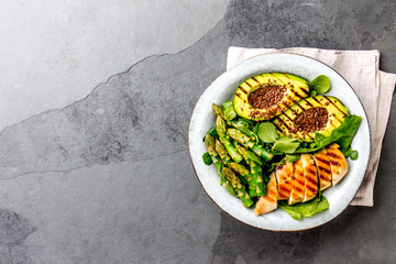 Healthy grilled chicken, grilled avocado and asparagus salad with linen seeds. Balanced lunch in bowl. Gray slate background. Top view