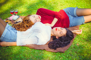 Two young pretty women with red and dark hair relax on picnic and enjoy life. Women's friendship as it is. Sisters rest on nature on the green lawn. Inspire lady with good mood at beautiful autumn day