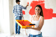 Young adult woman holding roller and paint for painting home
